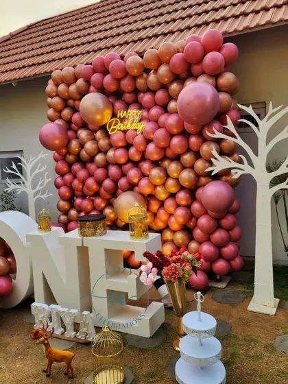 A stylish first birthday party with a large "ONE" marquee table. The backdrop is a full wall of metallic rose-gold balloons, creating a chic and modern look for a baby's milestone celebration.