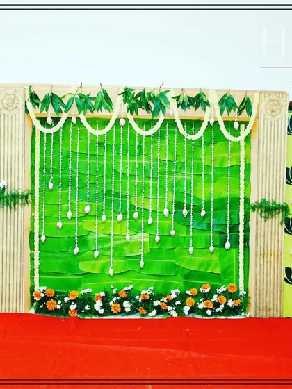 A full view of our traditional backdrop for a baby shower. It features a central panel of banana leaves, flanked by printed fabric with lotus motifs and jasmine flower hangings.