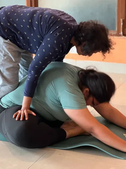 Two students work together in a seated forward bend. The support of a partner can help achieve a deeper and more beneficial stretch.