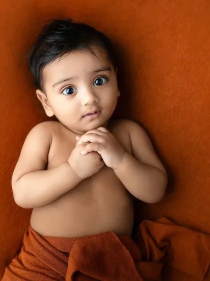 A six-month-old baby boy on his tummy, looking up with big, curious eyes. A classic pose that perfectly captures this developmental stage.