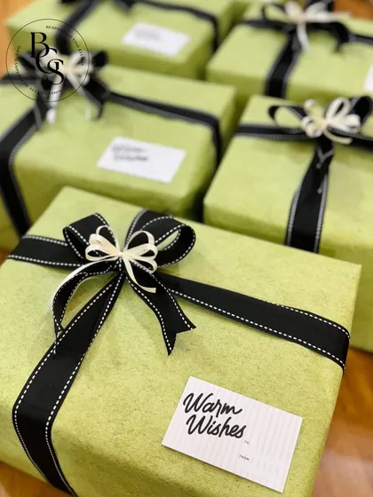 A close-up of gifts wrapped in a cheerful lime green paper. The black stitched-edge ribbon and "Warm Wishes" tag provide a sharp, modern contrast, making this a great choice for employee appreciation gifts.