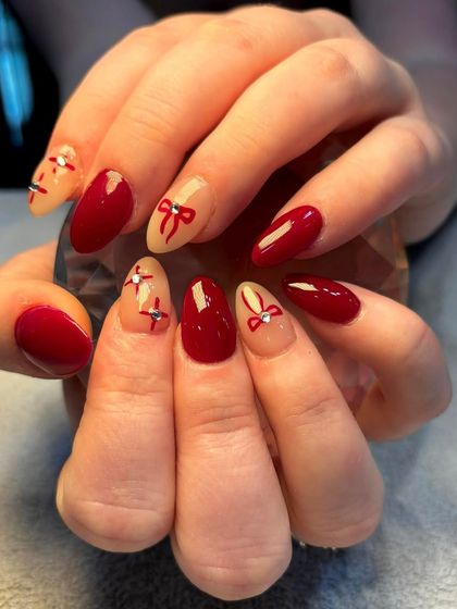 Let the Christmas nail trends begin. This festive set features a classic red polish with accent nails adorned with delicate, hand-painted bows and rhinestone details.