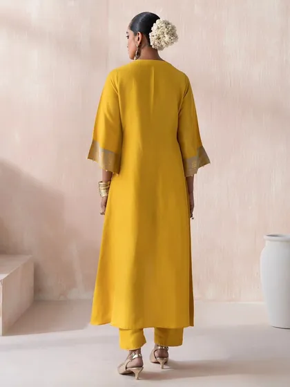 The back view of a mustard yellow kurta set from Saisha's "Firdaus" collection. This shot is styled to clearly display the outfit's cut, fit, and the subtle detailing on the sleeves.