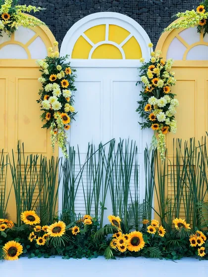 A charming photo backdrop with a white door and yellow window frames, adorned with cheerful sunflower arrangements.