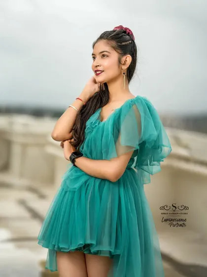 A beautiful three-quarter shot of the model in a flowing teal dress, looking off into the distance from a rooftop.