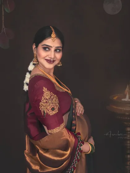 A stunning profile shot celebrating Akshaya Tritiya. The expecting mother is adorned in a beautiful Kancheepuram saree and traditional jewelry, with a lit lamp adding to the auspicious and warm atmosphere.