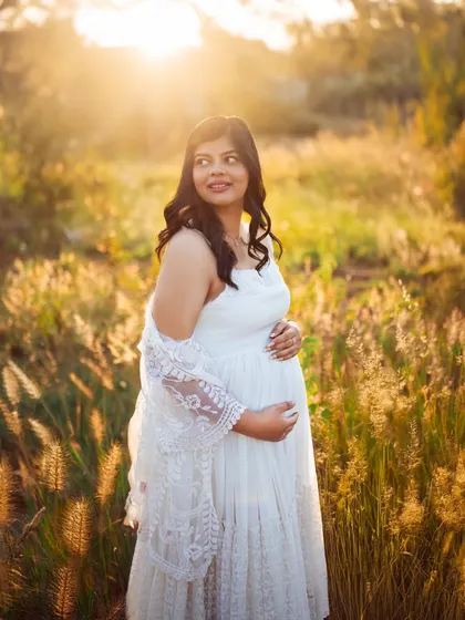 A close up shot capturing the mother's happy glow. The golden light of the sunset illuminates her, highlighting the joy and anticipation of this special time.