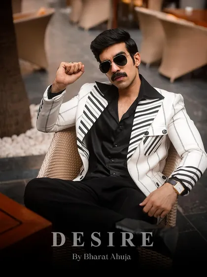 Power and poise. This seated pose highlights the structured shoulders and sharp lines of the white pinstripe blazer, a piece designed for the man in charge.