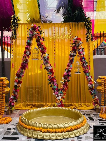 A unique 'M' shaped floral arch for a Haldi ceremony. I used bright yellow drapes and a mix of colorful flowers to create this personalized and grand backdrop.