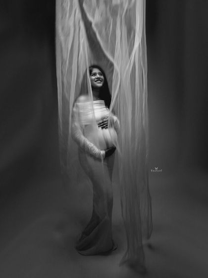 An ethereal black and white portrait. The mom-to-be is veiled in sheer, flowing fabric, creating a soft, dreamy, and almost sculptural image that is both delicate and strong.