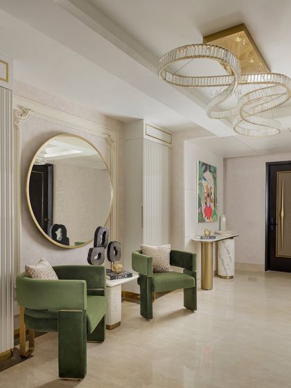 This foyer makes a statement. Sculptural green velvet chairs, a modern console, and a large round mirror are set against a backdrop of classic wall molding, offering a preview of the grand design within.