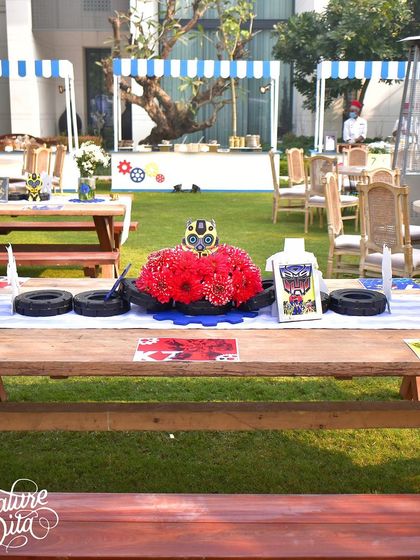I designed these rustic picnic tables with centrepieces made of red flowers, tires, and Transformer masks. It's a creative way to blend natural elements with a mechanical theme.