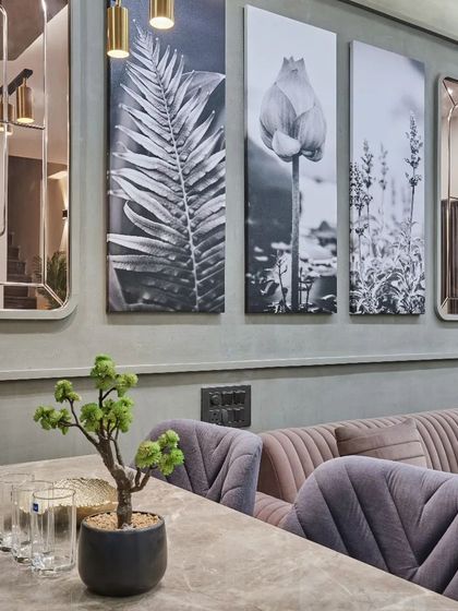 The dining and living area of this Vadodara residence is defined by a sophisticated color palette of dusty rose and grey, with botanical art prints adding a natural touch.