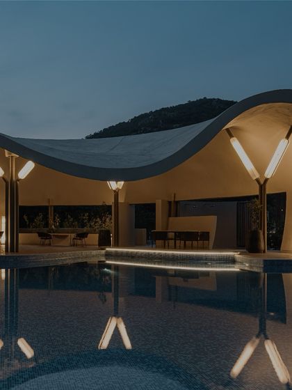 A closer view of the pool and covered lounge area at night. The subtle under-ledge lighting and warm interior lights create an inviting glow, ensuring the space feels intimate and connected to the tranquil water even after sunset.