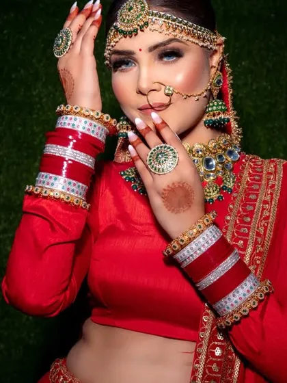 A close-up of a bride with stunning blue eyes, wearing a traditional red outfit and heavy jewelry.