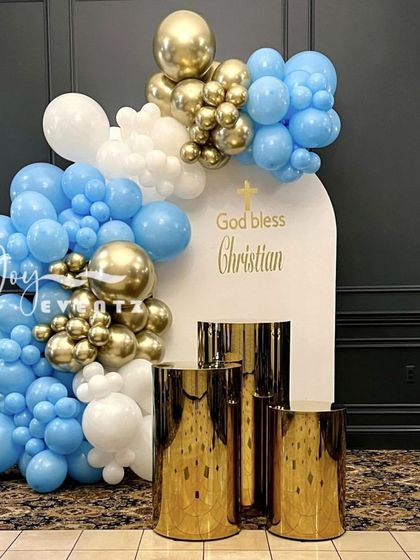 A classic blue, white, and gold balloon decoration for a boy's First Holy Communion. The setup is completed with reflective gold plinths and a personalized backdrop, perfect for photos.