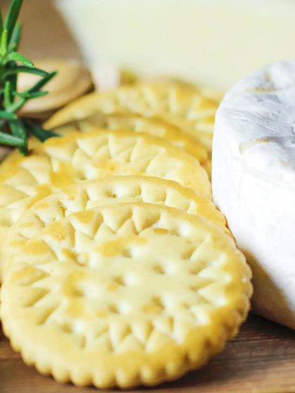 A macro shot of crisp, savory crackers placed next to a wheel of soft cheese, garnished with fresh rosemary. This image emphasizes the importance of texture and fresh ingredients.