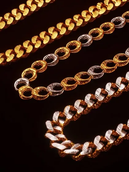 A studio photograph displaying three different styles of gold and silver chains against a stark black background. This comparison shot is excellent for catalogs, allowing customers to see the variations in design.