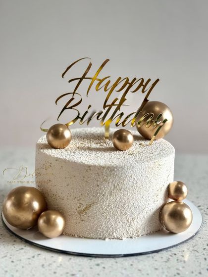 A simple yet elegant birthday cake with a textured white finish and scattered gold chocolate spheres.