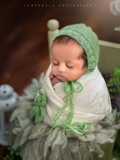 A beautifully composed shot of a newborn boy in a green knit bonnet, sleeping soundly with a tiny matching teddy bear.