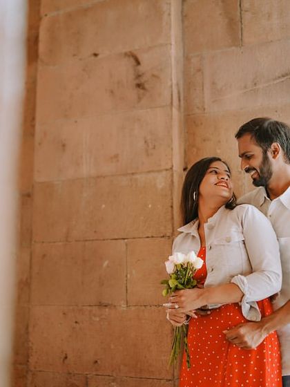 A sweet and gentle moment between a couple near historic architecture, with the bride holding a bouquet of white flowers.