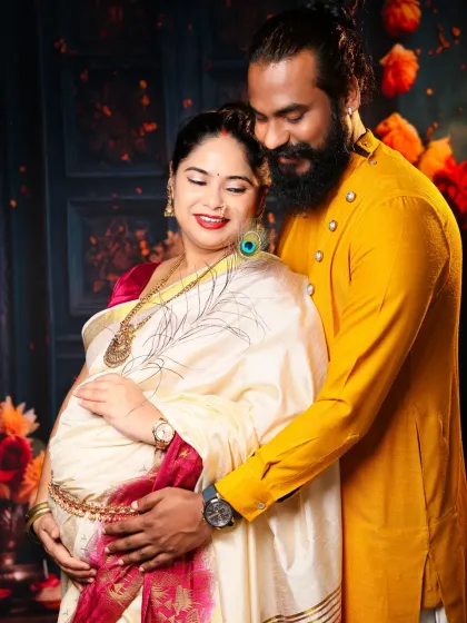 A close-up shot filled with love and tradition. The intricate details of the saree and jewelry are highlighted as the couple shares a tender moment, their hands on the baby bump.