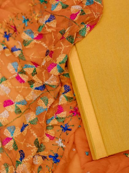 A detail shot of a yellow wedding album cover, resting on a beautifully embroidered orange fabric.