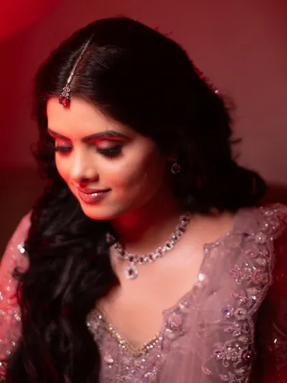 A soft and romantic bridal portrait. The red lighting creates a warm, intimate mood, focusing on the bride's gentle smile and elegant jewelry.