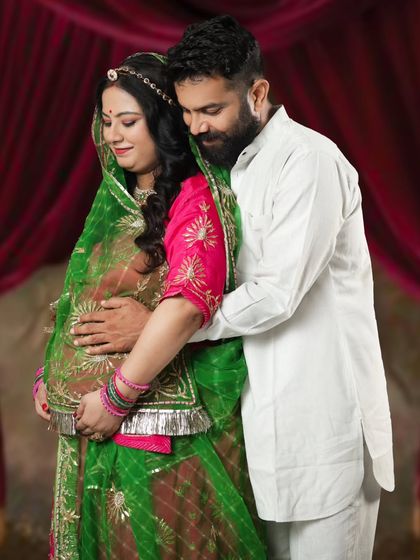 A couple dressed in traditional Rajasthani attire shares a warm embrace. The rich colors of the poshak and the studio backdrop create a regal and intimate portrait.