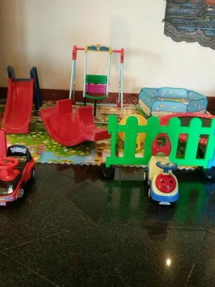 This is an example of an indoor play area setup on a hard floor. It features a slide, swing, rocker, ride-on cars, and a foldable ball pit, all enclosed by a colorful fence.