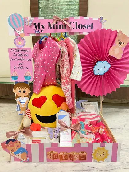 Our "My Mini Closet" hamper is a bundle of joy, featuring an emoji pillow, baby care products, and a selection of adorable pink outfits for the new arrival.
