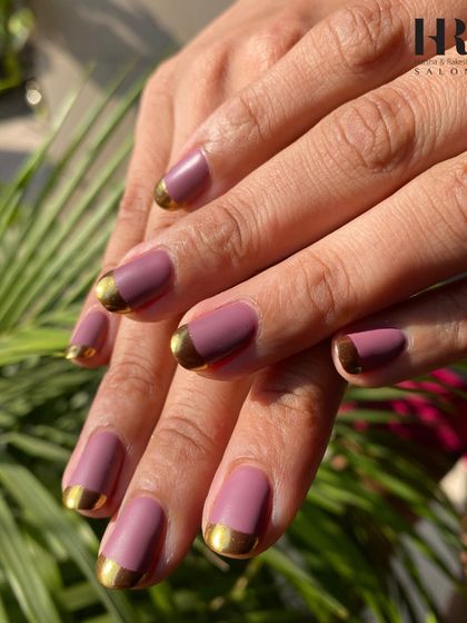 A modern twist on a classic. This chic manicure features a matte mauve polish with a glossy, metallic gold French tip, creating a sophisticated and trendy look that's perfect for any occasion.
