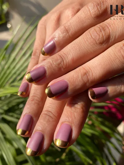 A modern twist on a classic. This chic manicure features a matte mauve polish with a glossy, metallic gold French tip, creating a sophisticated and trendy look that's perfect for any occasion.