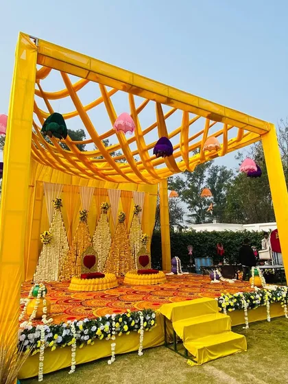 A bright and sunny Haldi stage, featuring a lattice-work yellow canopy and a backdrop made of marigold and tuberose strings.