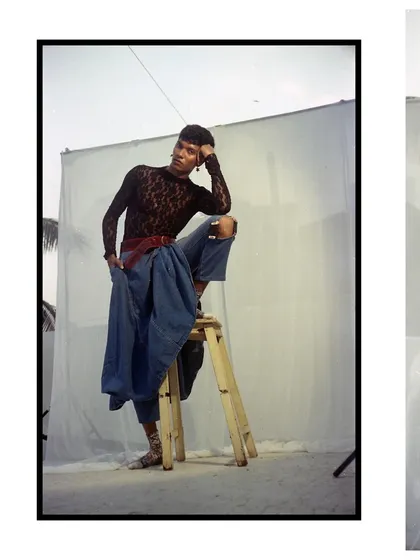 A portrait captured on 35mm film, showcasing a raw and unfiltered aesthetic. The composition, featuring a simple stool and backdrop, highlights the androgynous styling and the unique texture of analogue photography.