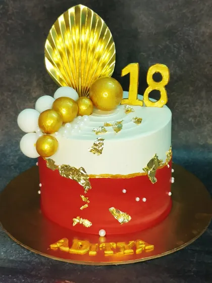 An 18th birthday cake with a bold red and white design. This chocolate hazelnut cake is decorated with a golden palm leaf and spheres.