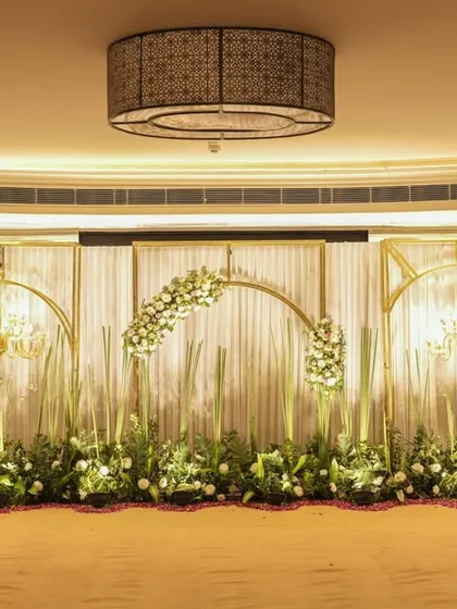 A full view of the elegant stage setup from the entrance. The symmetrical design with golden frames and floral arches creates a grand and picturesque focal point for the event.