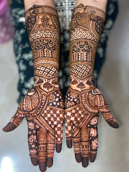 A full-hand design featuring peacocks near the elbows and a mix of floral and geometric patterns covering the rest of the arms and hands.