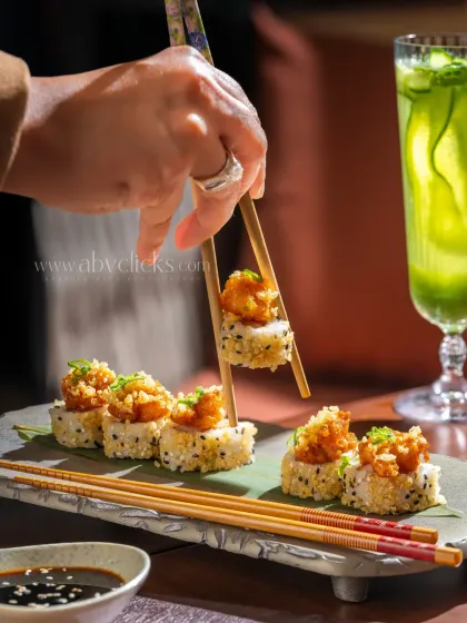 An action shot of chopsticks picking up a piece of sushi at Camo, Noida, with a refreshing drink in the background.