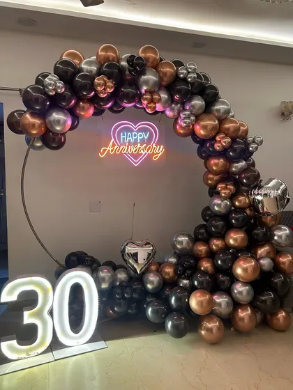 A full view of the stylish 30th anniversary balloon decoration. The large marquee '30' numbers are illuminated, standing next to the circular frame adorned with a modern balloon arrangement.