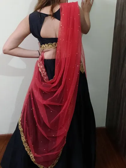 The back view of the black lehenga set, showing the stylish keyhole back of the blouse and the way the red net dupatta can be draped.
