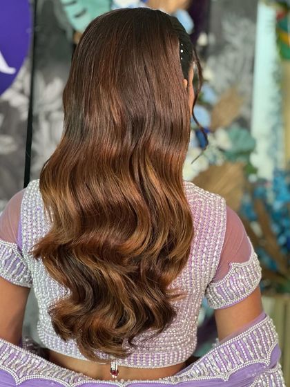 The back view of a beautiful, voluminous ponytail with rich, caramel highlights. The hair is styled in glossy waves, creating a luxurious and eye-catching look for any special occasion.