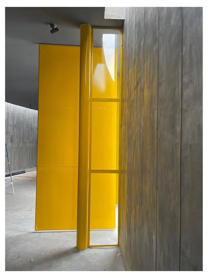 A detail of a large, pivoting door in a bold yellow, set against board-formed concrete walls. This contrast between raw, textured material and a clean, colorful industrial element is a signature of my approach to modern public architecture.