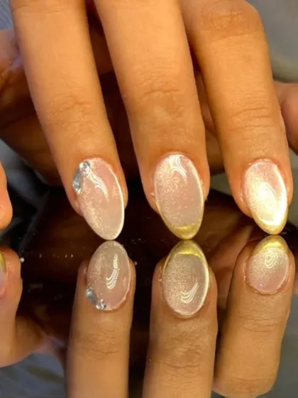 An elegant French manicure with a gold chrome tip over a shimmery cat-eye base, accented with a single rhinestone.