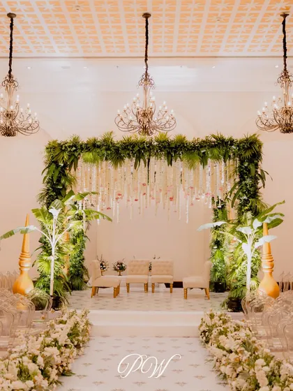 An indoor mandap that brings the outdoors in. We used lush green walls, banana plants, and a ceiling of hanging florals to create a tropical oasis inside the banquet hall.