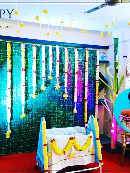 A beautiful home setup for an Annaprasanna or naming ceremony. The decor features a woven mat backdrop, hanging flower strings, and a decorated cradle.