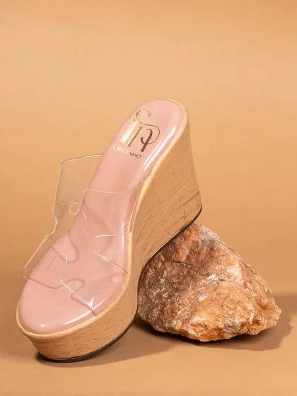 A product-only shot of a clear wedge sandal, creatively propped against a rock. This artistic composition highlights the shoe's unique design and silhouette.