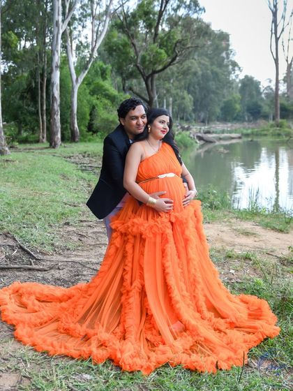 A romantic couple's portrait by a lake, with the dad-to-be embracing his partner from behind.