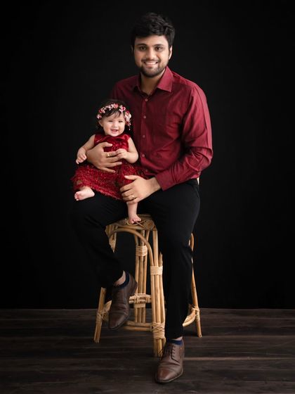 A father and daughter portrait against a dramatic black background. The rich red outfits create a stunning contrast, resulting in a powerful and elegant image.