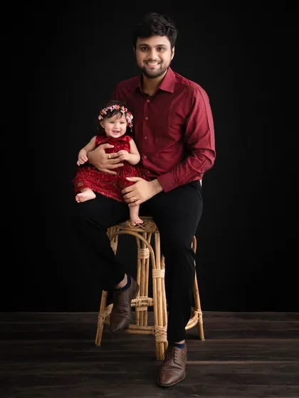 A classic father and daughter portrait. The deep red of their matching outfits creates a warm and loving image against the moody, dark background.